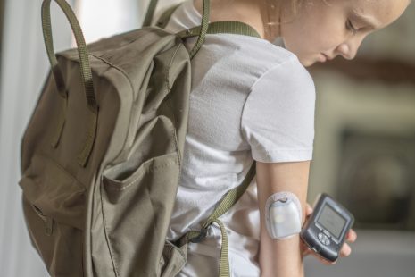 A fourteen year old Caucasian girl reads her blood sugar level by placing her reader next to her pump in her arm as she is about to leave for school.