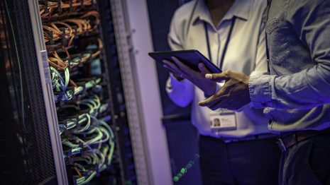 Photo of two unrecognizable information technology engineers talking about server next to a collection of cables in the server room.